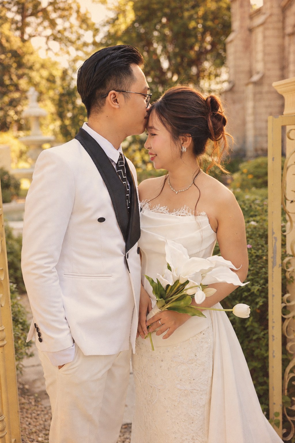 Chú rể hôn trán cô dâu trong khuôn viên xanh